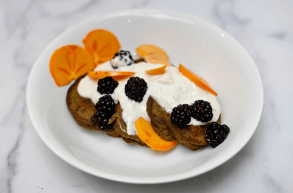 a white plate with 3 pancakes and topped with cream and fruit