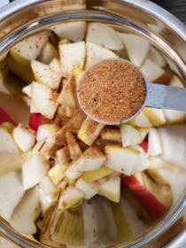 cinnamon being added to a bowl of chopped apples