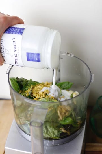 Cream being poured into a food processor with basil in it