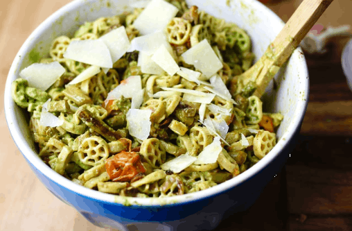 a bowl of pasta tossed with pesto and topped with parmesan shavings