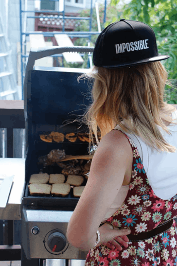 a woman grilling with a black hat that says impossible on it