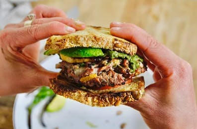 a hand holding a half eaten sandwich on a plate