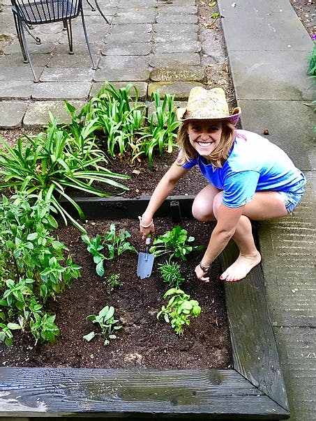 a woman crouching in a garden planting plants
