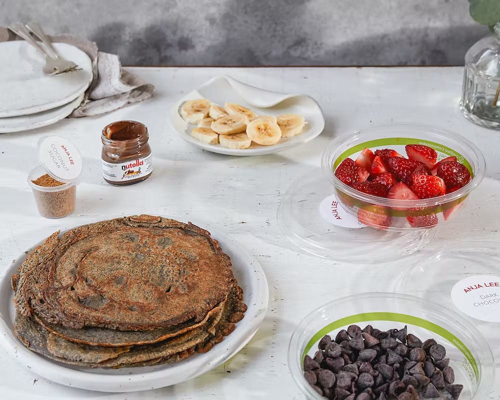 a table topped crepes and crepe toppings including fruit and chocolate chips