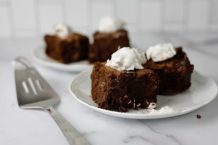 two plates with two brownies on each, all topped with whipped cream next to a silver spatula