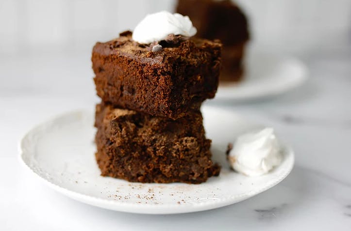 two brownies stacked on top of each other on a white plate with whipped cream