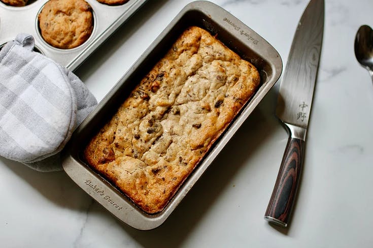 a pan of banana bread next to a knife and oven mitt
