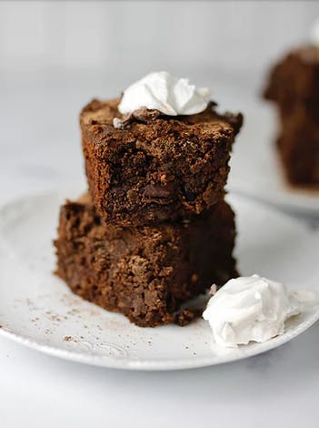 two brownies stacked on top of each other on a white plate with whipped cream