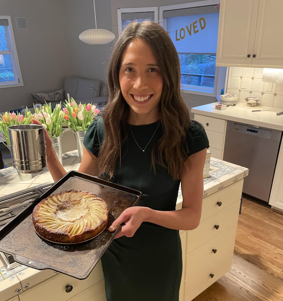 a woman smiling in a kitchen holding up a tarte on a baking sheet