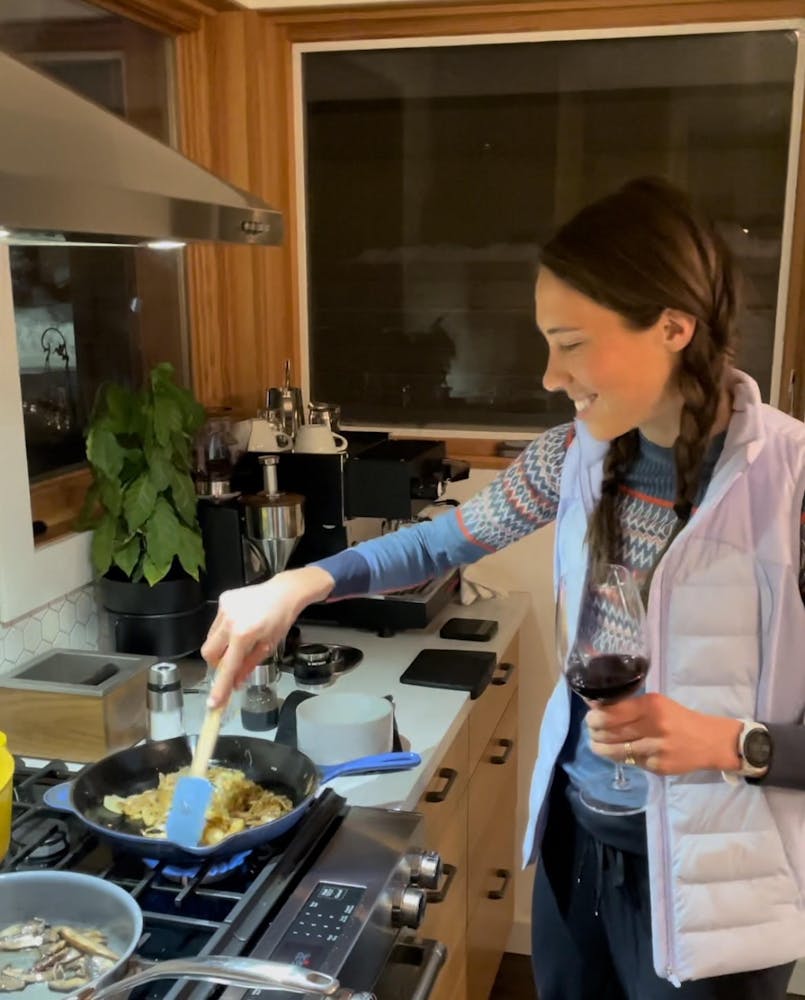 a woman cooking over the stove holding a glass of red wine