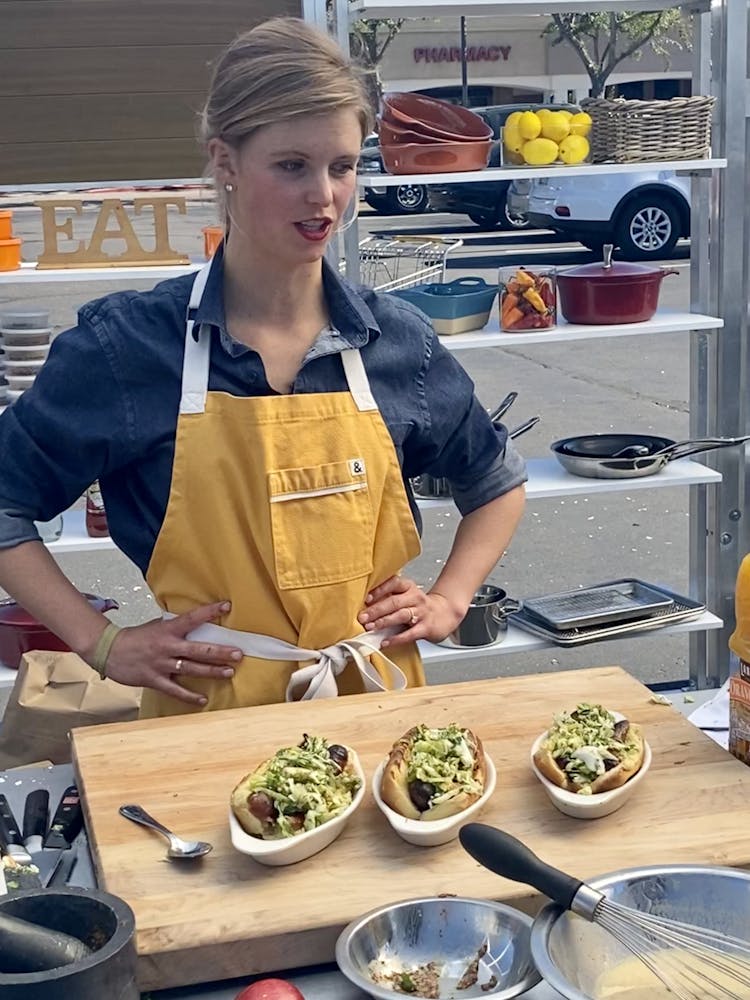 a woman sitting at a table with 3 plates of hot dogs