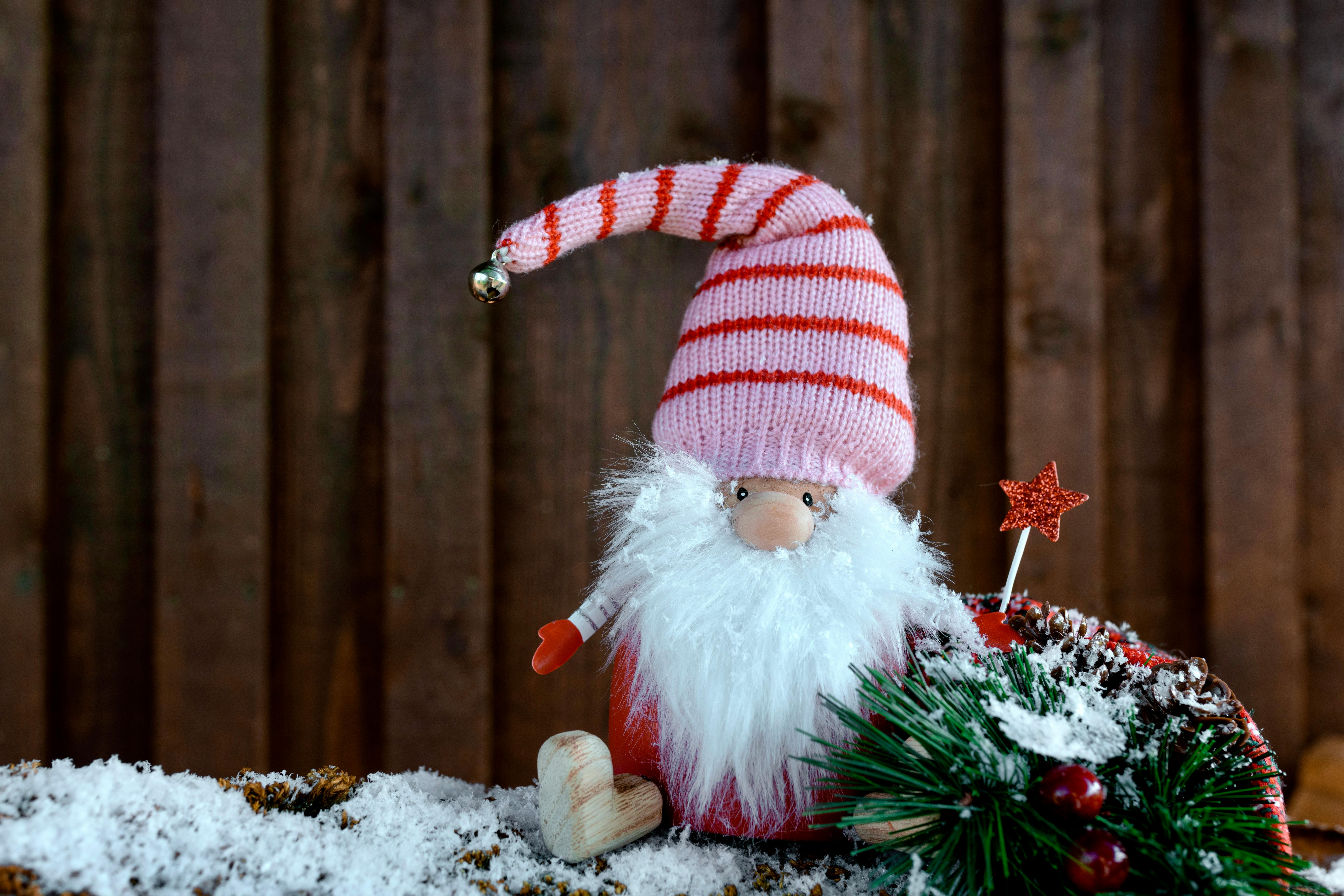 a small santa figurine with beard and hat sitting in front of a wooden background