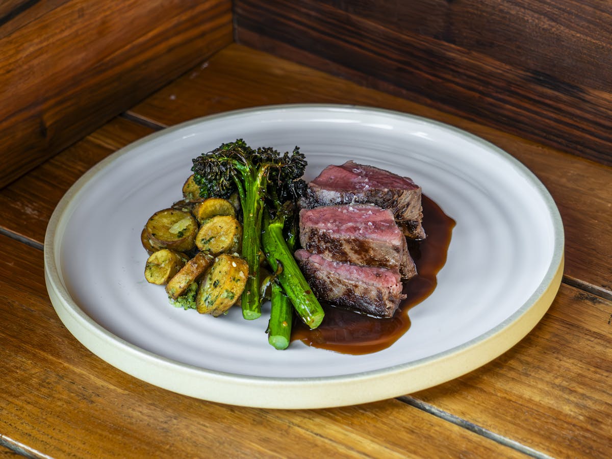 a plate of food / steak sitting on top of a wooden table