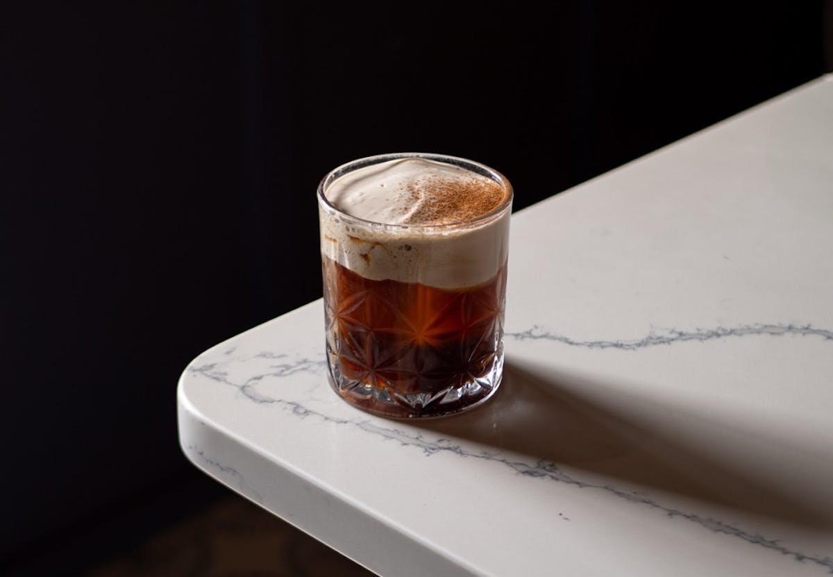 Craft cocktail with foam topping served in a rocks glass on a marble table