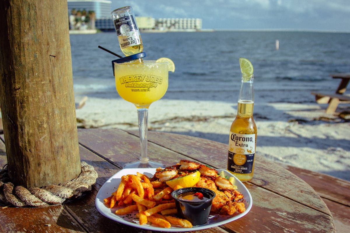 a plate of food with a beer and margarita facing the beach