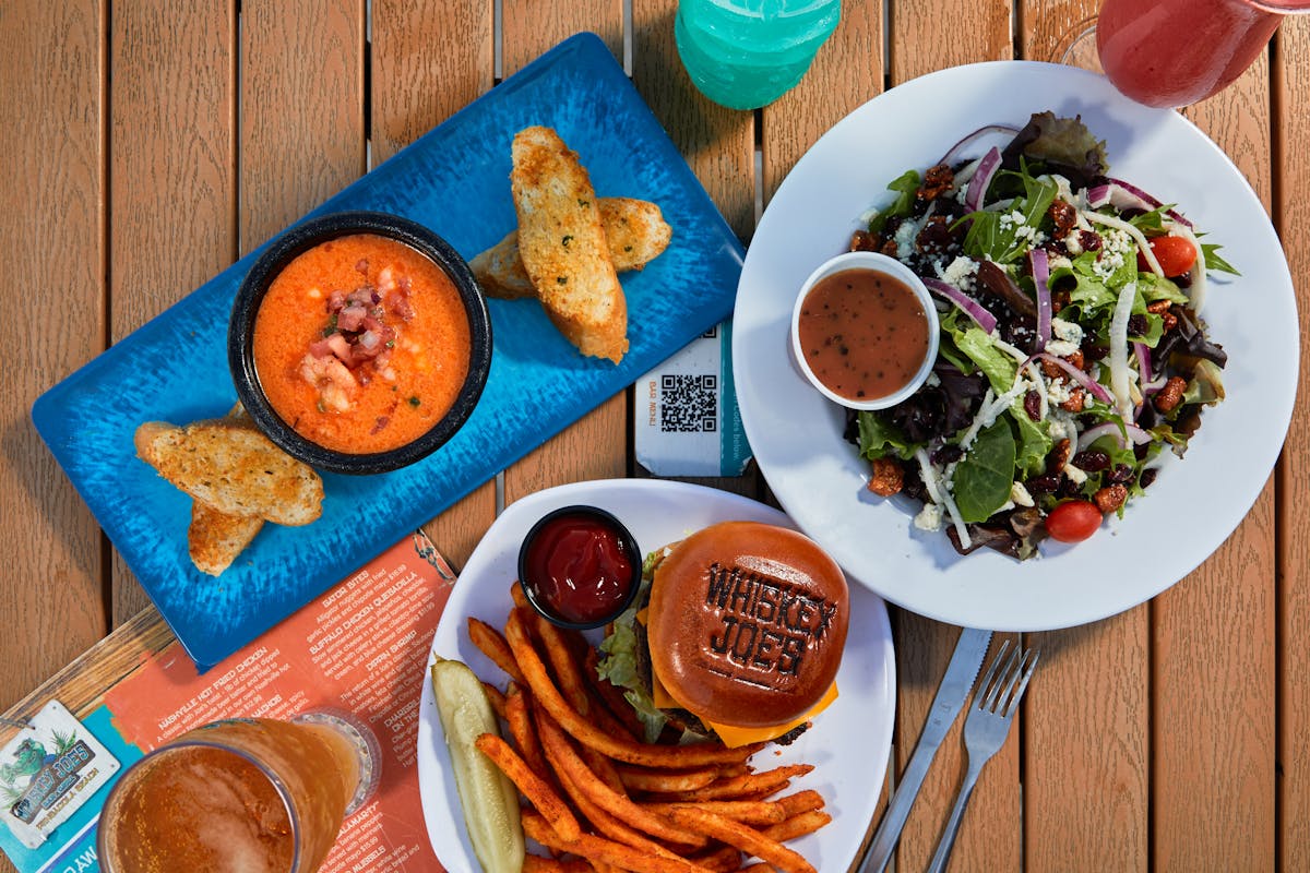overhead shot of a salad, burger and soup on a wooden table