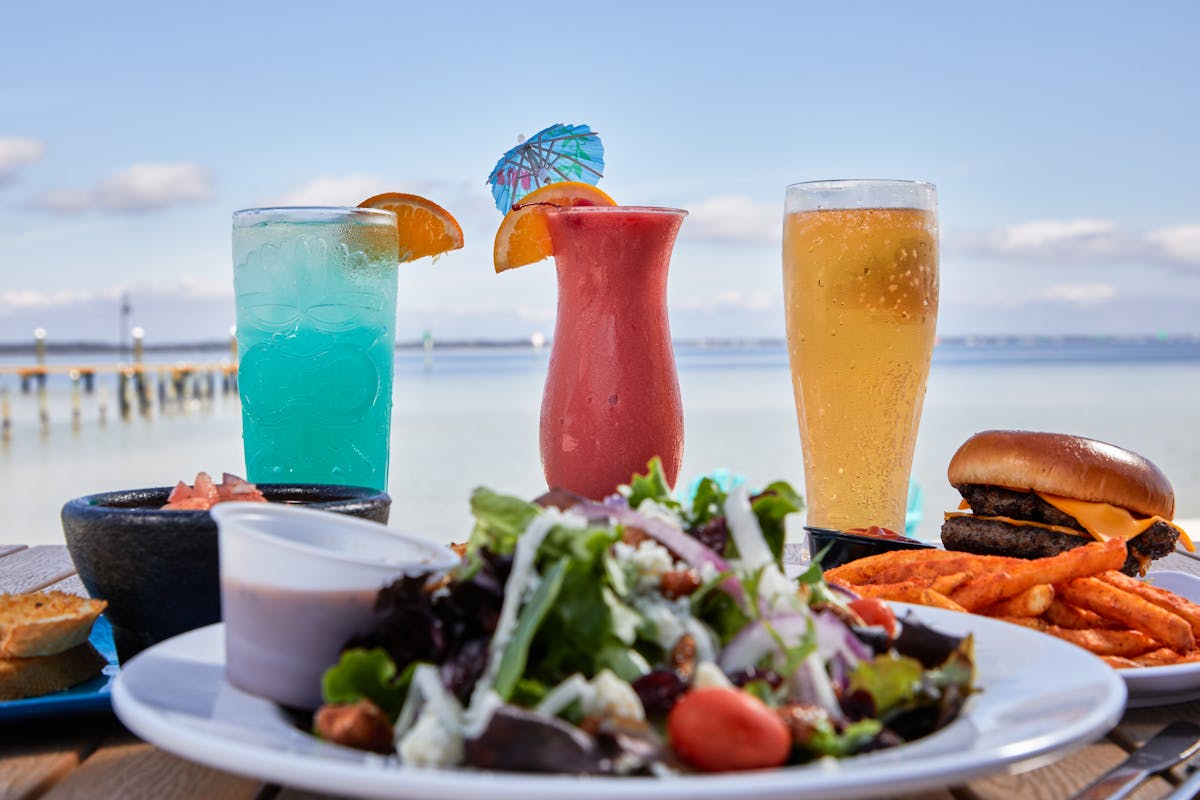 three cocktails lined up behing a plate of salad overlooking the beach