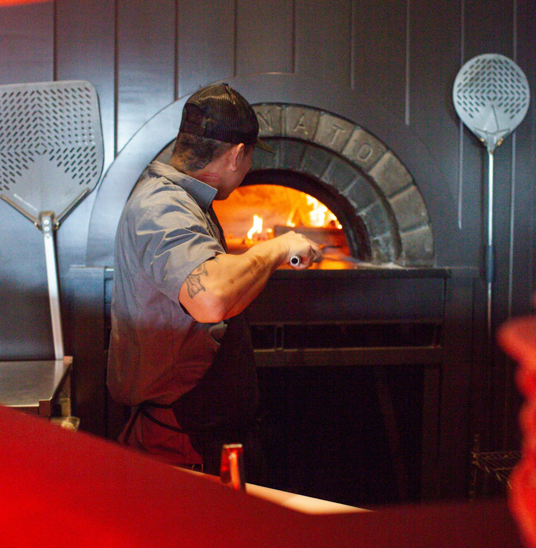 a man pulling a pizza to the oven