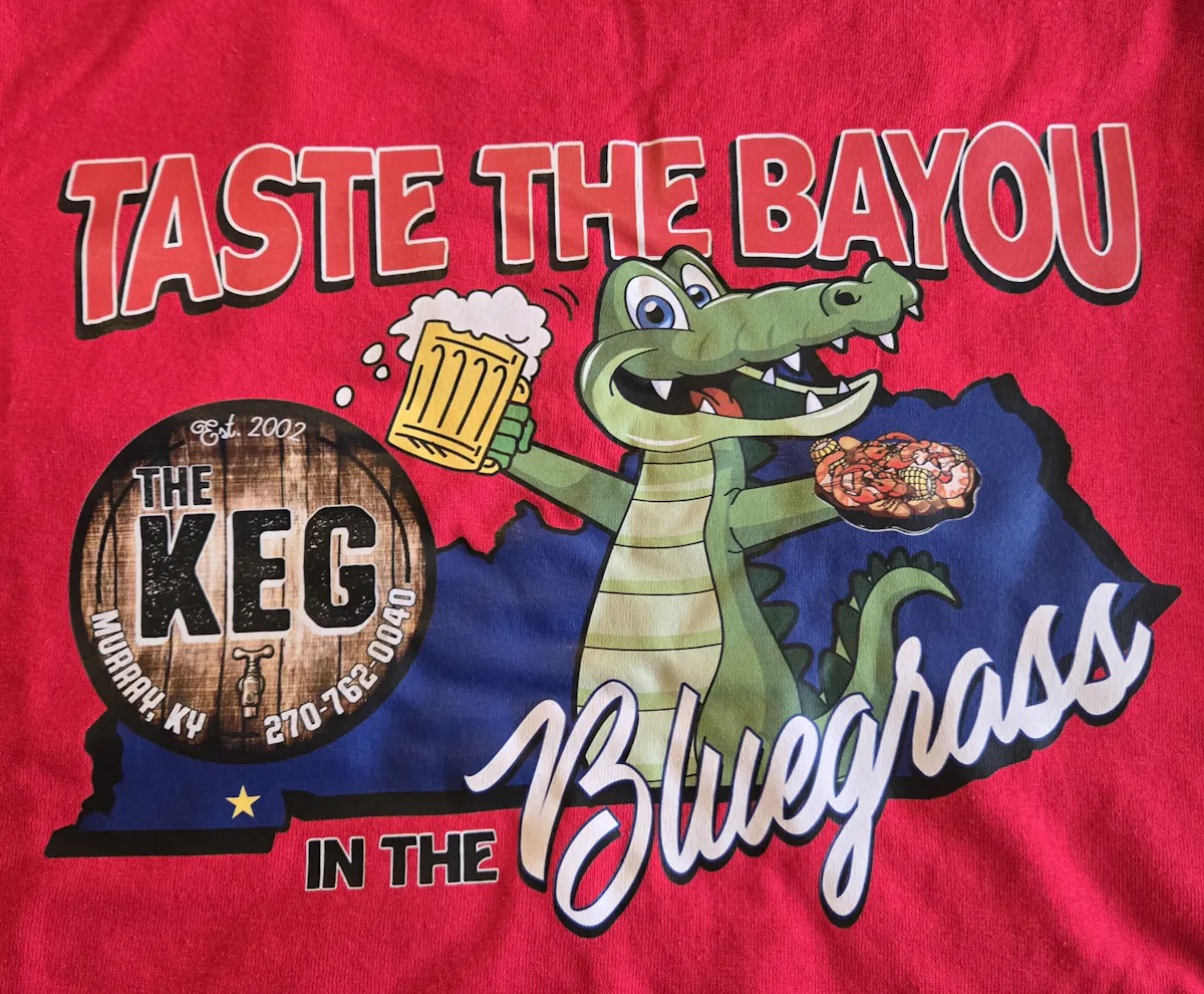a red shirt with a cartoon alligator holding a beer and a sign