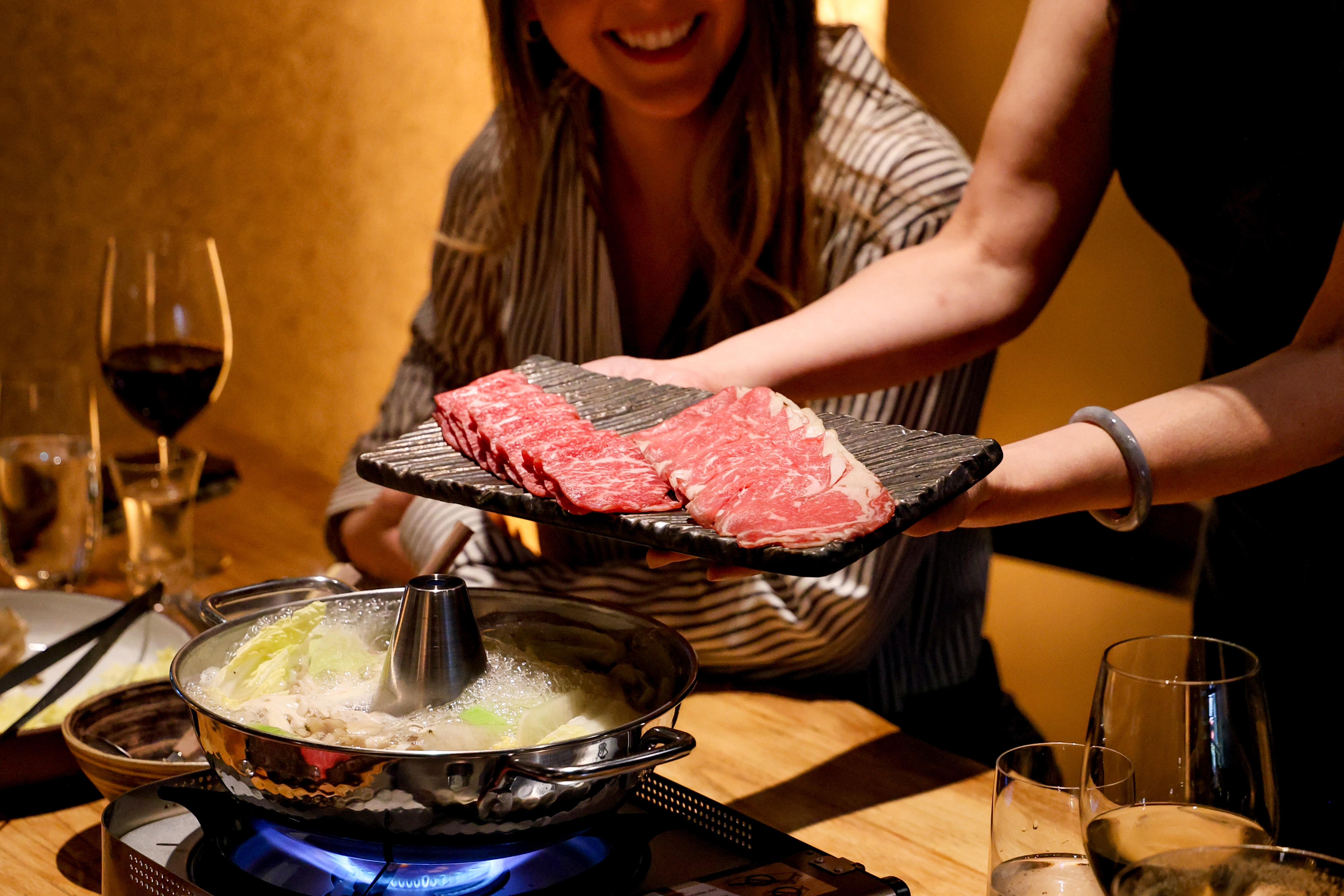 a woman holding a tray of meat over a pot of food