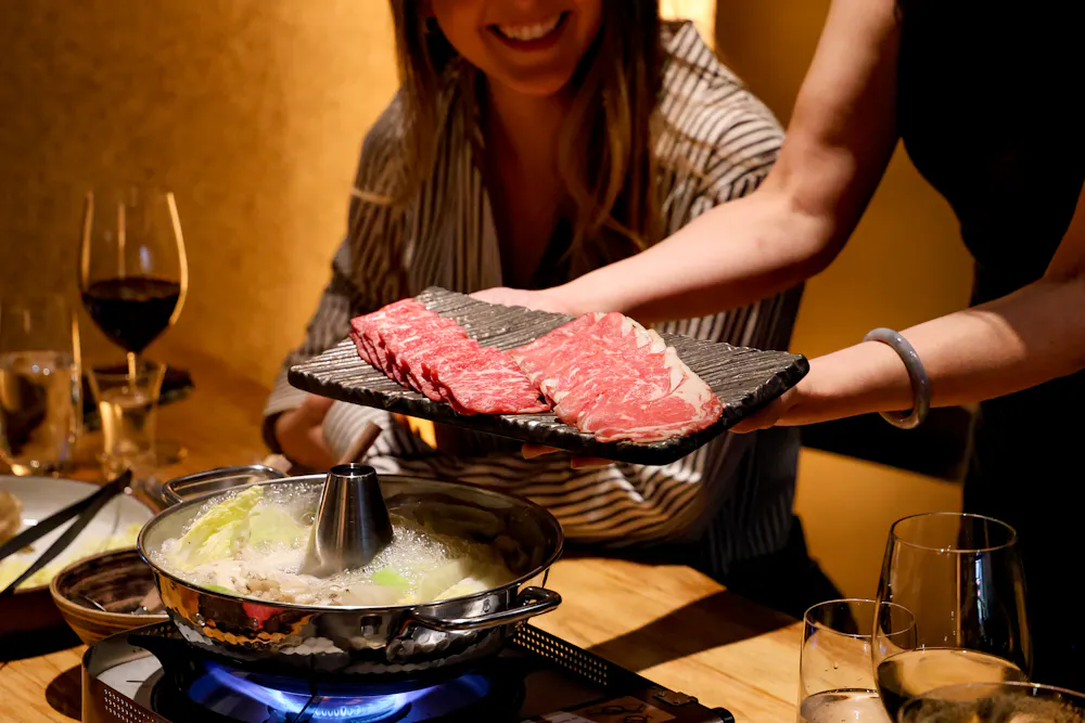 a woman holding a tray of meat over a pot of food
