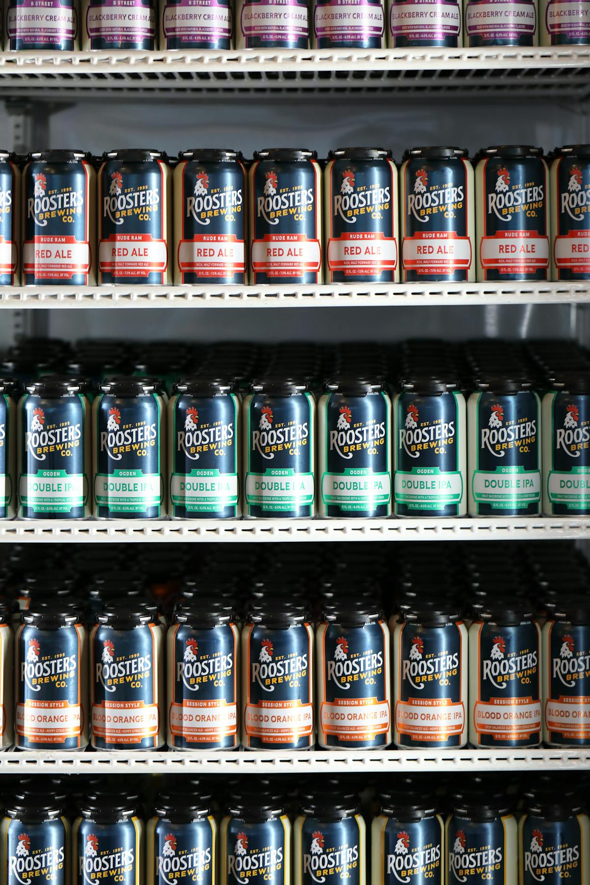 Various cans of Rude Ram Red Ale on three rows of shelves