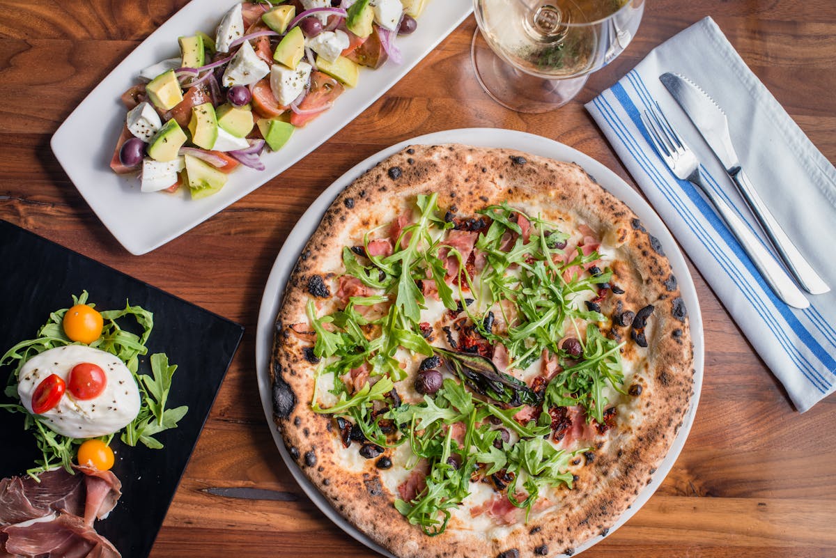 a pizza sitting on top of a wooden table with a plate of food