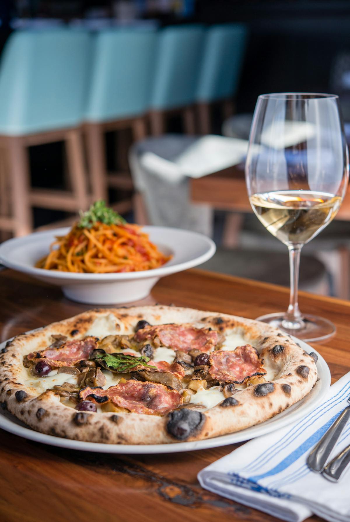 a pizza, spaghetti plate and a wine glass on a table