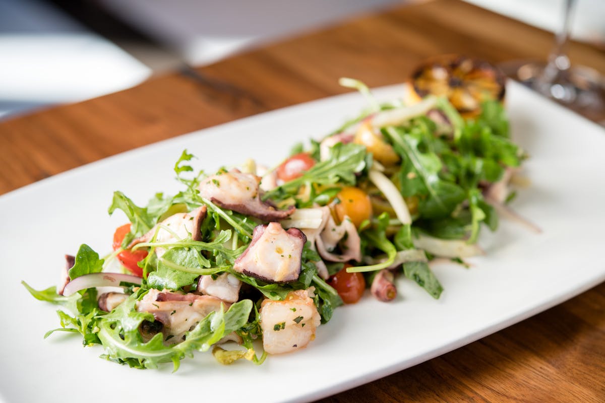 a white plate topped with a green salad on top of a wooden table