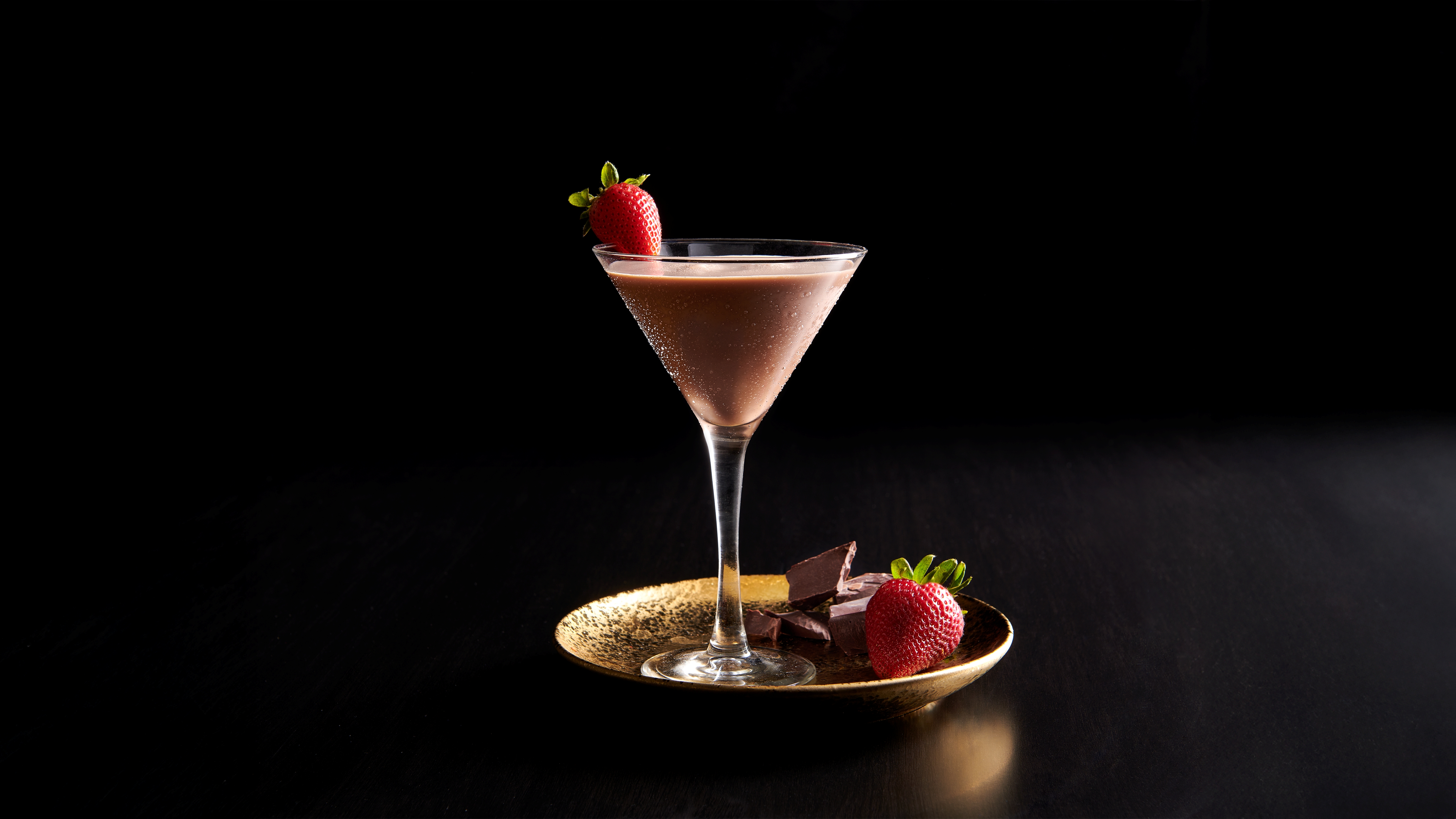 a glass of chocolate drink with strawberries on a gold plate