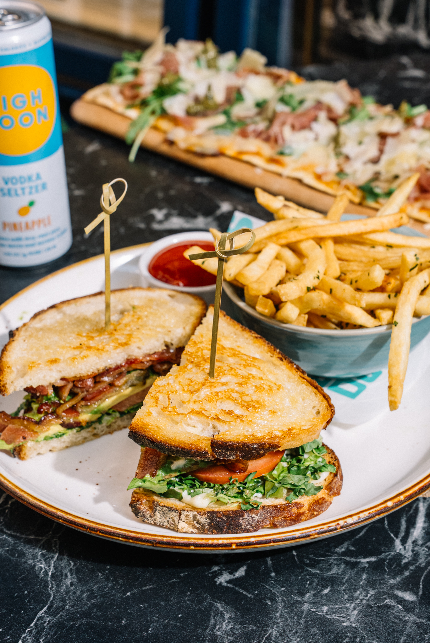 BLAT sandwich on a plate with fries and beverage in the background