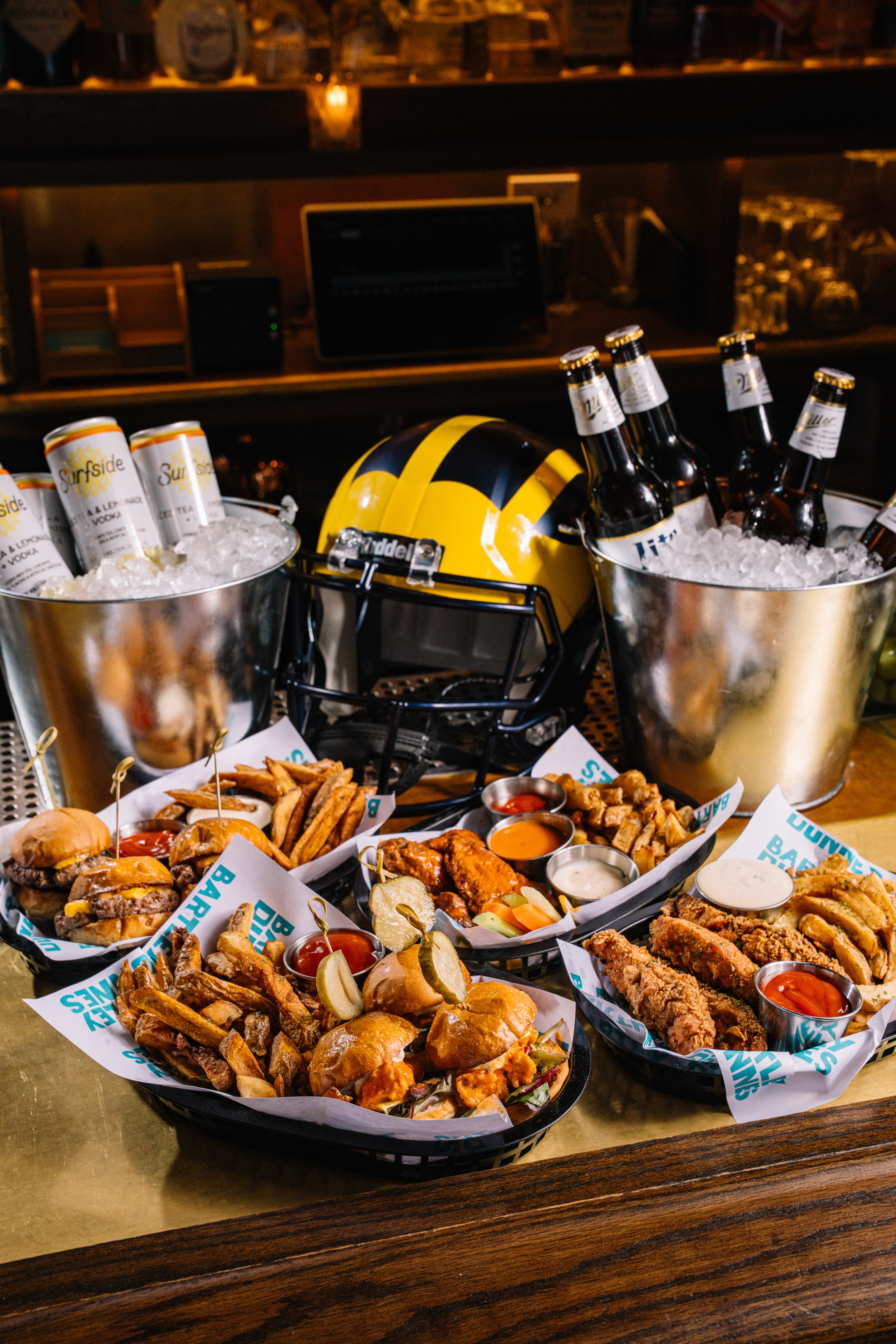 football sunday photo with beer buckets, food in front including wings, fries, tenders and sliders