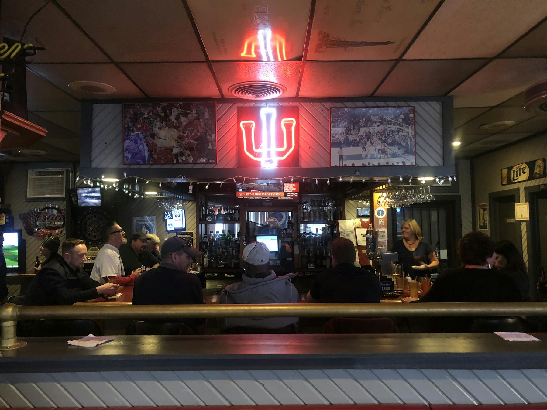 Darkly lit bar with light up IU sign on wall.